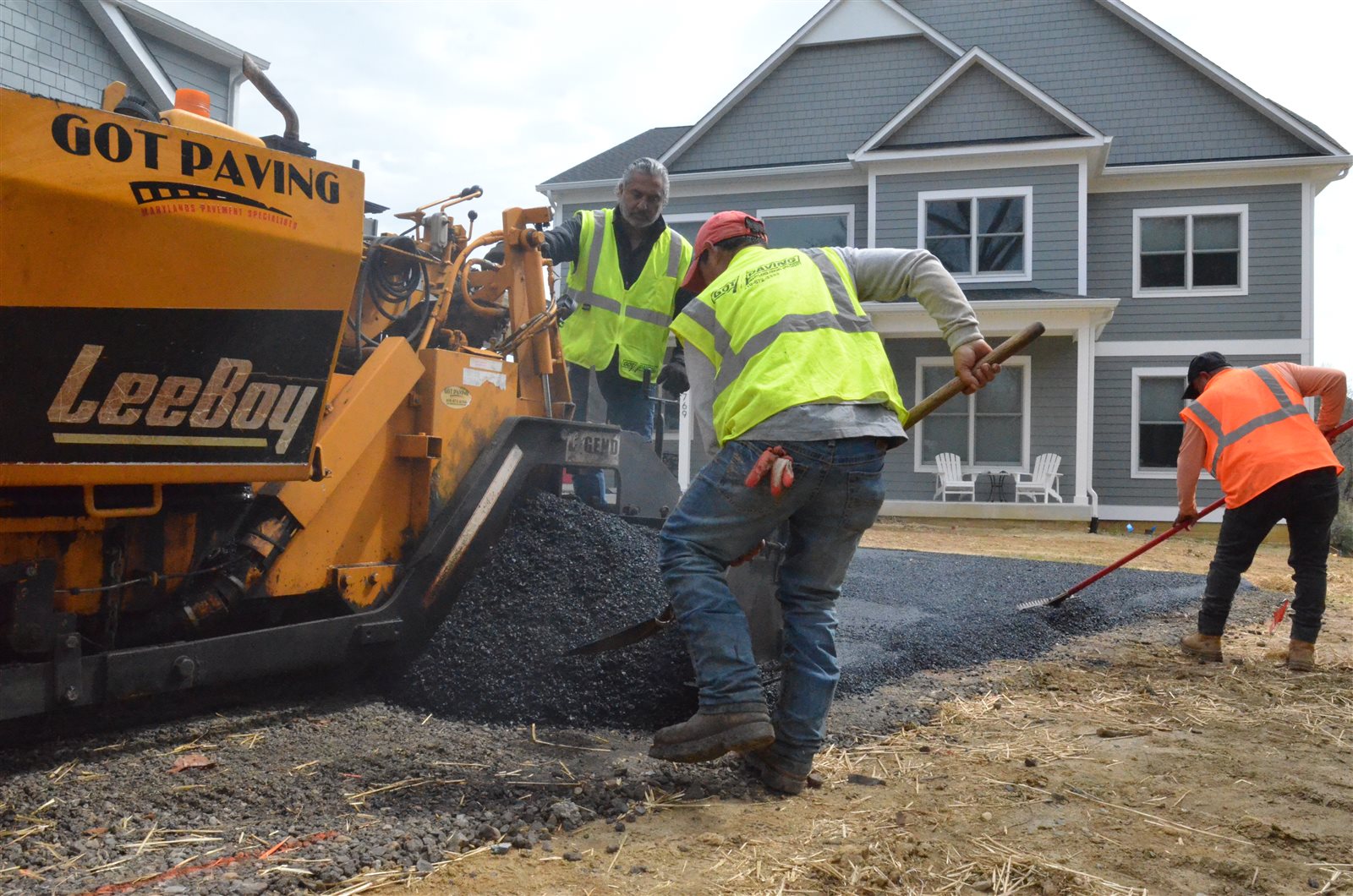 Paving crew laying a fresh asphalt driveway at a home